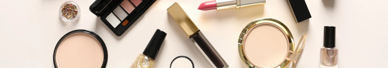 Composizione di prodotti cosmetici come rossetti, ciprie, palette di ombretti e profumi disposti insieme.