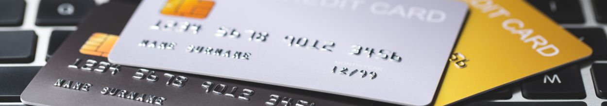 Tre carte di credito elettroniche con chip (color antracite, argento e oro) parzialmente sovrapposte sulla tastiera di un computer portatile